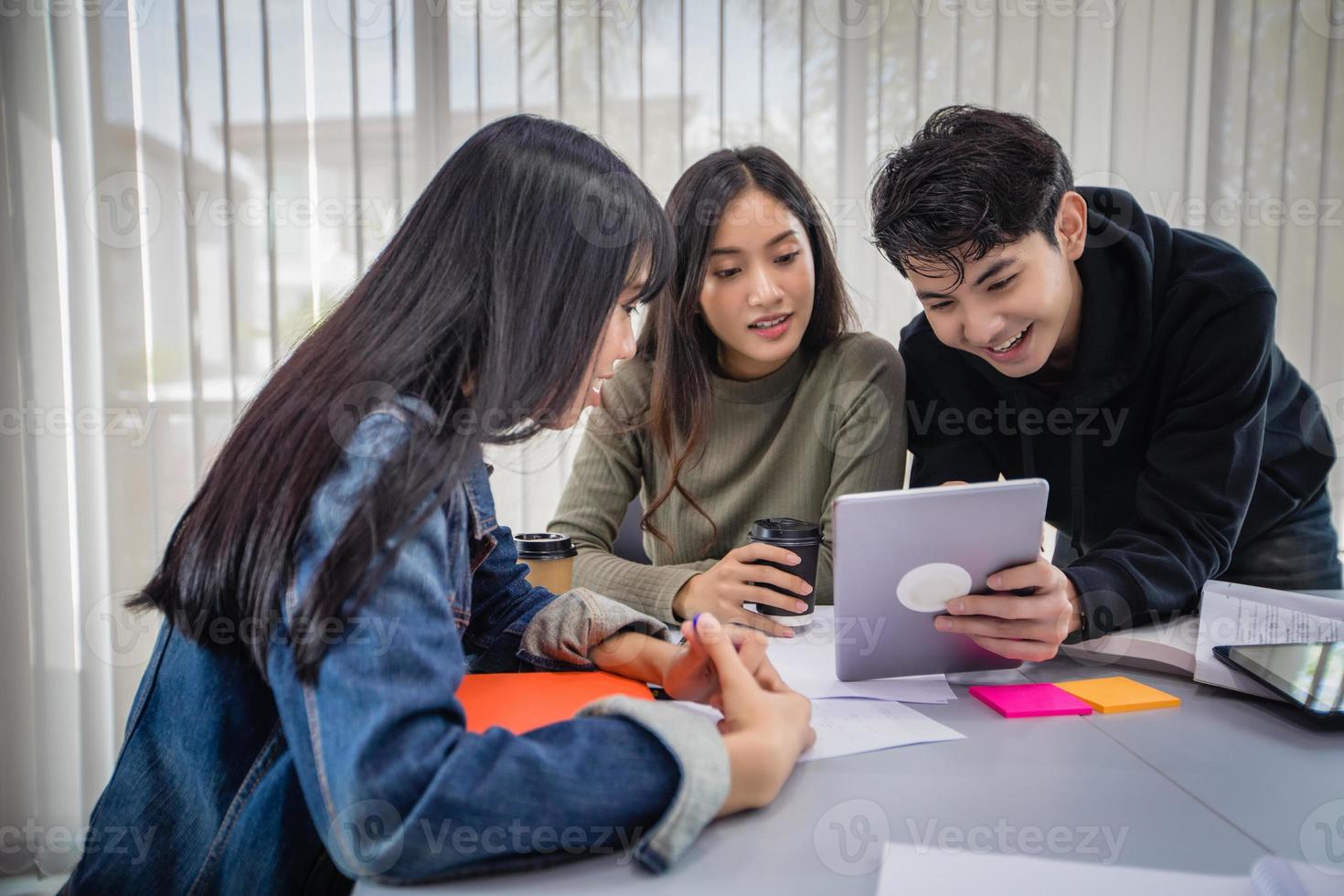 los estudiantes asiáticos del grupo sonríen y leen libros y usan un cuaderno para ayudar a compartir ideas en el trabajo y el proyecto. y también repasar el libro antes del examen foto