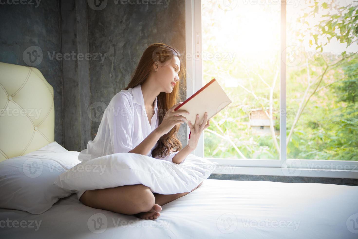 mujer asiática lee su cama por la mañana en casa en un día relajante. foto