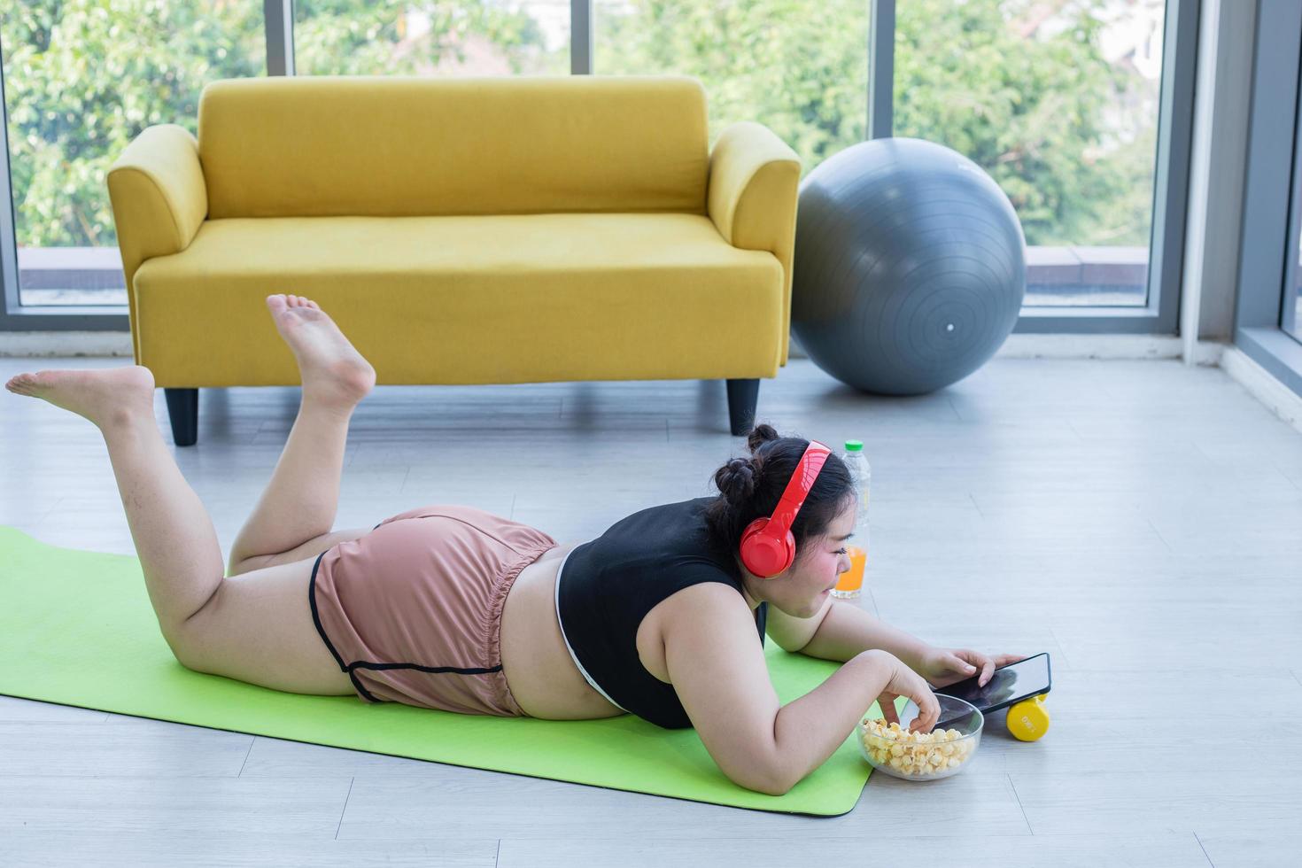 Asian overweight woman using tablet and. wearing headphone for listening music and She is exercising at home ,Asian girl enjoy eating food and popcorn photo