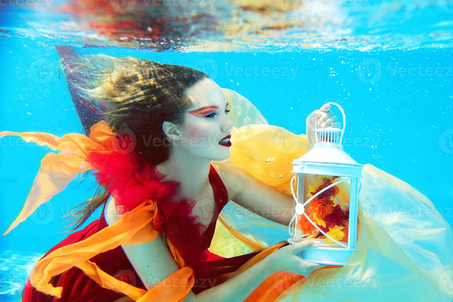 Underwater fashion portrait of beautiful blonde young woman in red dress with lamp photo