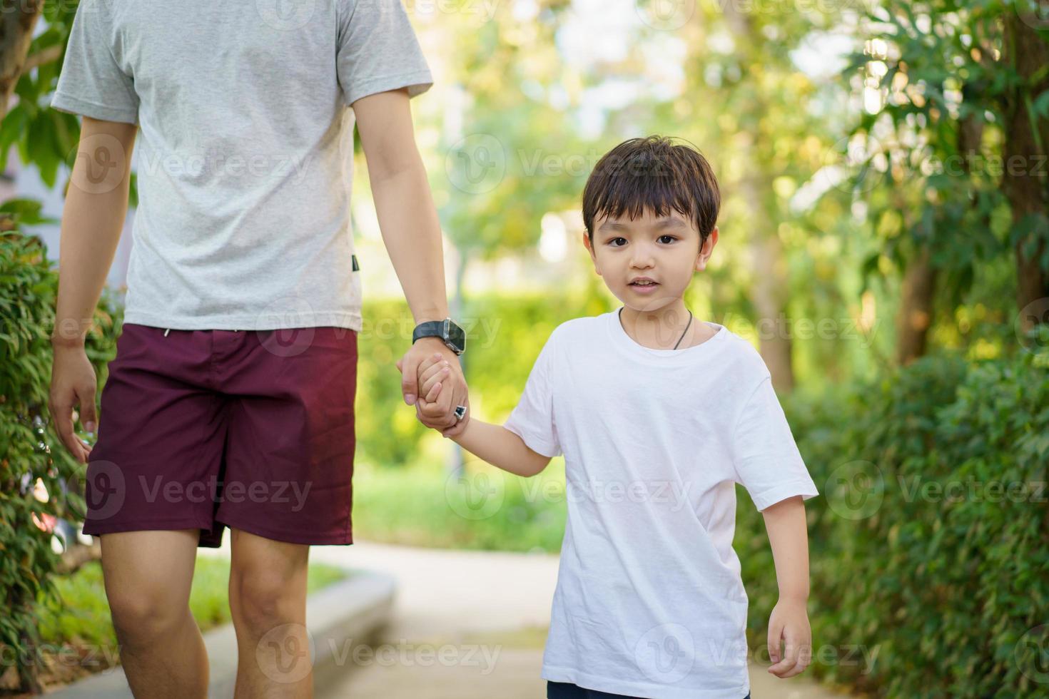 Happy Asian little boy enjoy playing and walking at the park with daddy close up, Asian boy have a beautiful smiling while looking at his father. Little boy portrait at the park and playground. photo