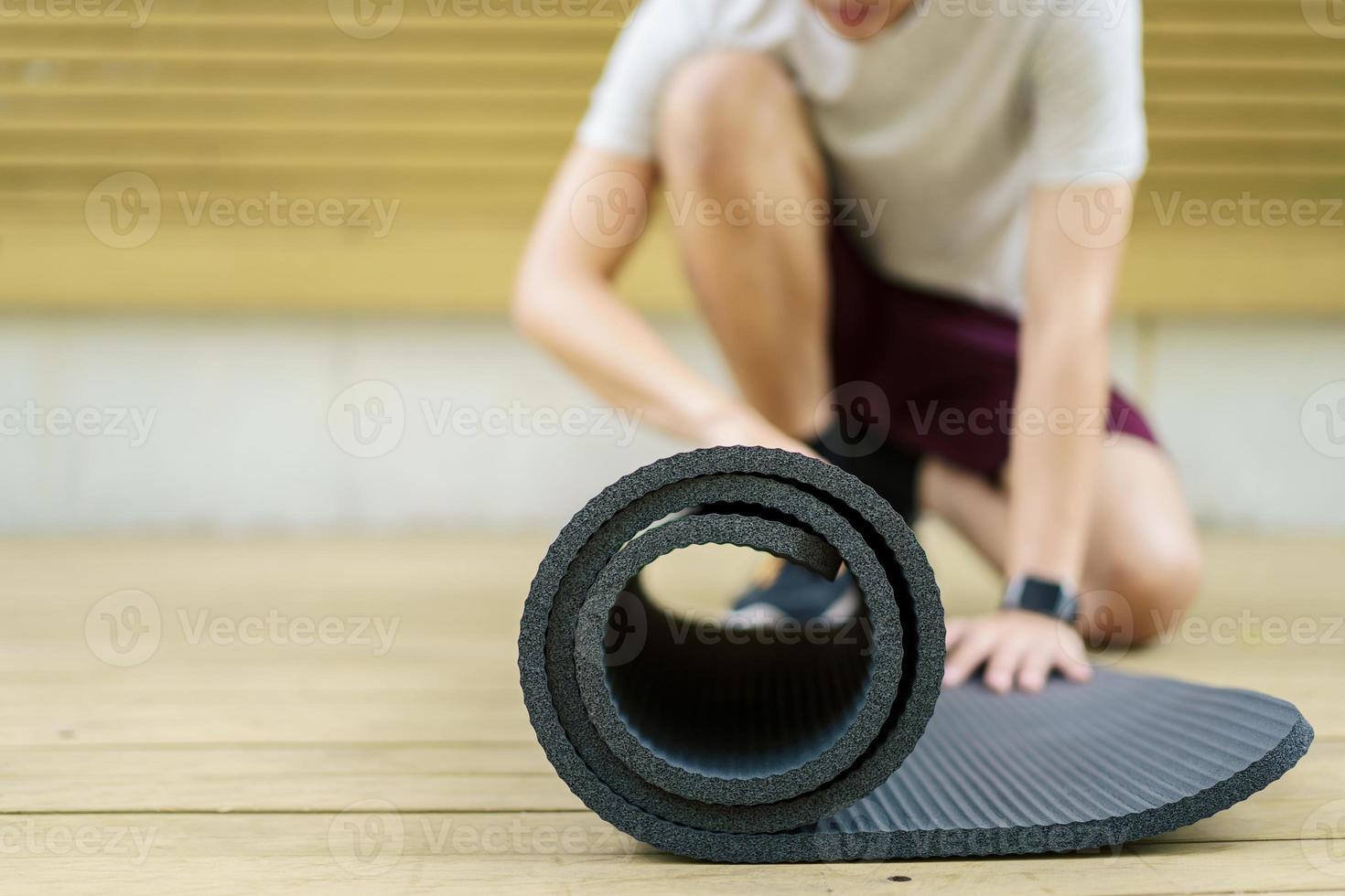 un deportista asiático activo desenrolla una colchoneta de ejercicio en el suelo, un cuerpo sano y en forma de un deportista asiático que prepara una colchoneta de yoga para el peso corporal y el ejercicio cardiovascular. foto