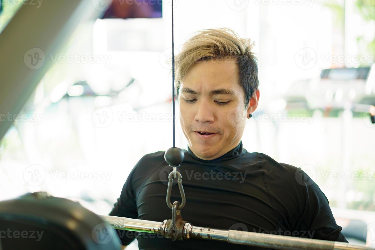 un joven deportista asiático activo practica entrenamiento con pesas en el gimnasio usando una máquina de pesas. hombre haciendo un ejercicio de entrenamiento con pesas para la construcción de músculo y cuerpo. personas sanas - equilibrio trabajo-vida foto