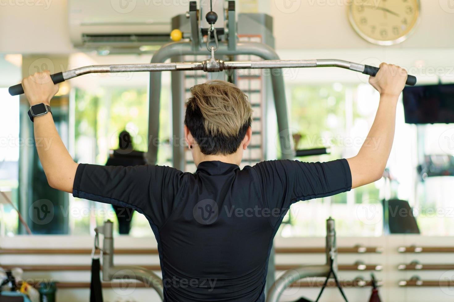 Active young Asian sportsman practice weight training in the gym by using weight pulldown machine. Man doing a weight training exercise for muscle and body building. Healthy people - work life balance photo