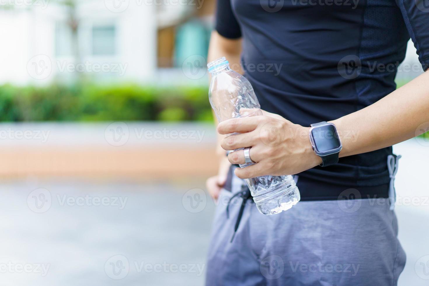 Active Asian sportsman relaxing and drinking a water in bottle after outdoor running or workout. Asian man drink a water during the break from exercise. A healthy man trying hard for cardio workout. photo