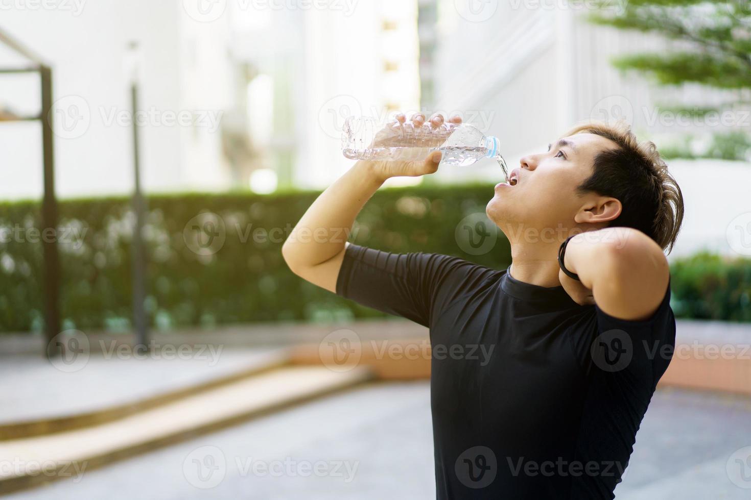 Active Asian sportsman relaxing and drinking a water in bottle after outdoor running or workout. Asian man drink a water during the break from exercise. A healthy man trying hard for cardio workout. photo