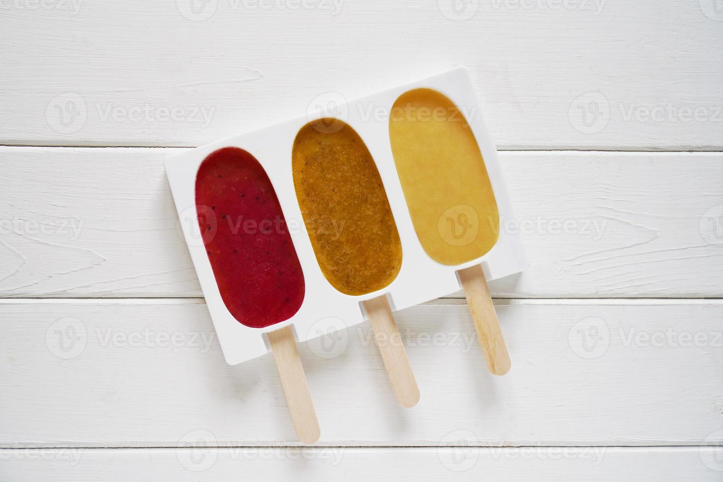 Tres paletas de batido de frutas diferentes en un molde de silicona reutilizable para paletas heladas foto