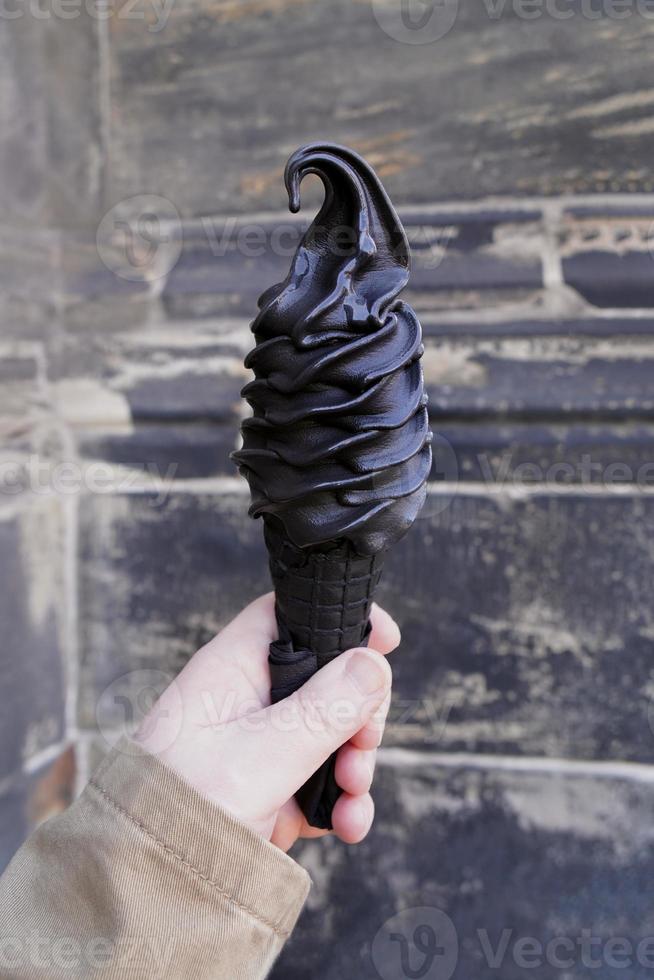 hand holding black soft serve ice cream cone made with activated charcoal photo