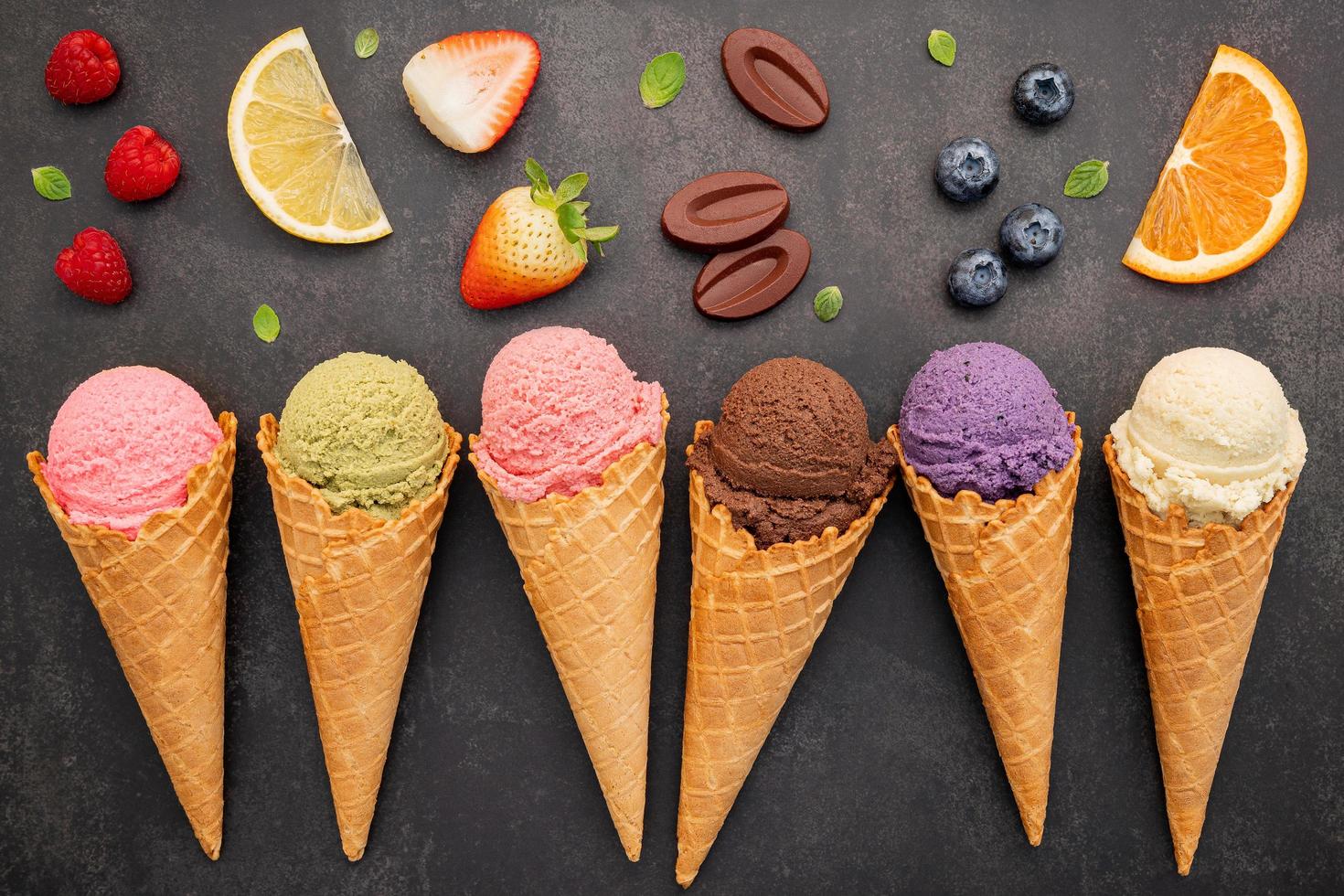 Colección de conos de helado planos laicos sobre fondo de piedra oscura. Cono de helado crujiente en blanco con espacio de copia para el diseño del menú de dulces. foto