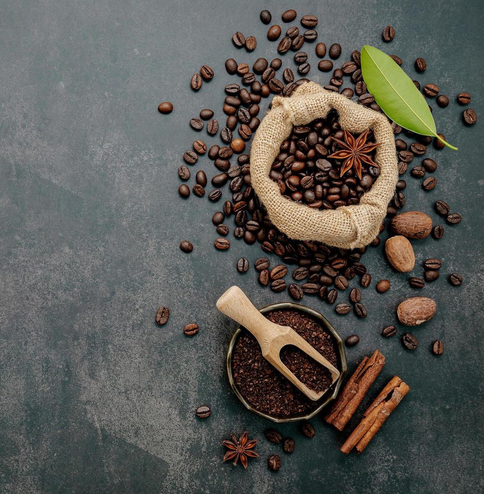 Roasted coffee beans with coffee powder and flavourful ingredients for make tasty coffee setup on dark stone background. photo