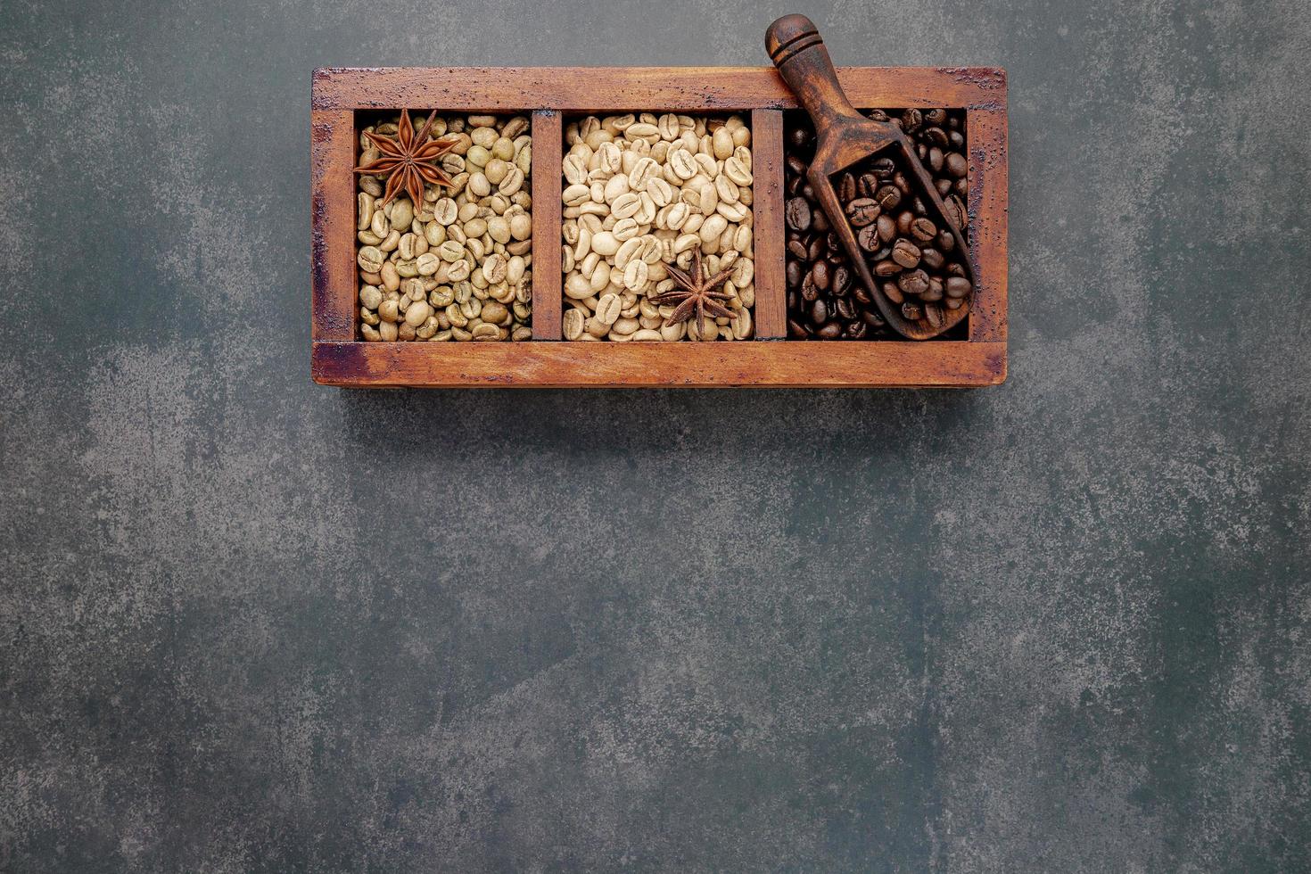 Green and brown unroasted and dark roasted coffee beans in wooden box with scoops setup on dark concrete background. photo