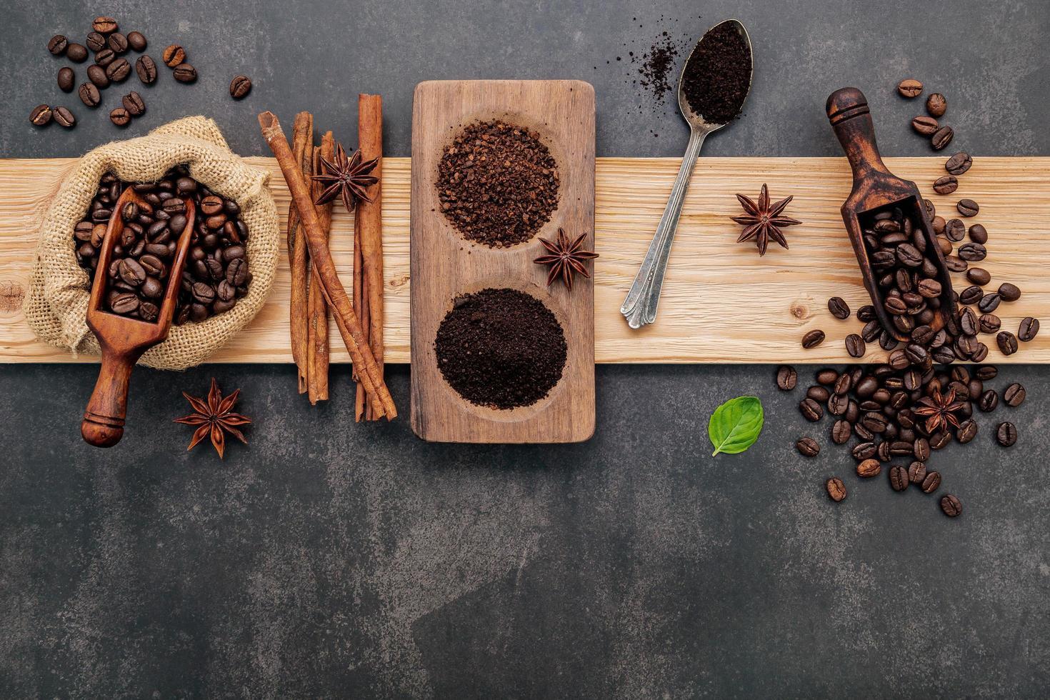 Roasted coffee beans with coffee powder and flavourful ingredients for make tasty coffee setup on dark stone background. photo