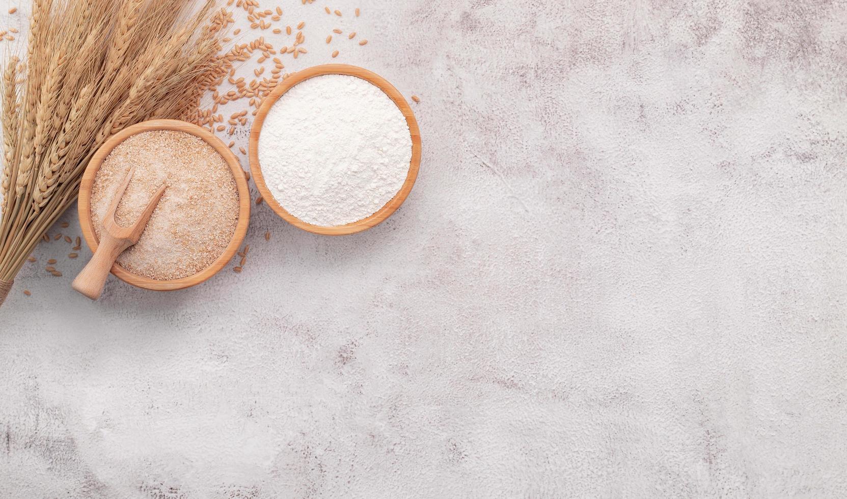 Wheat grains , brown wheat flour and white wheat flour in wooden bowl set up on white concrete background. photo