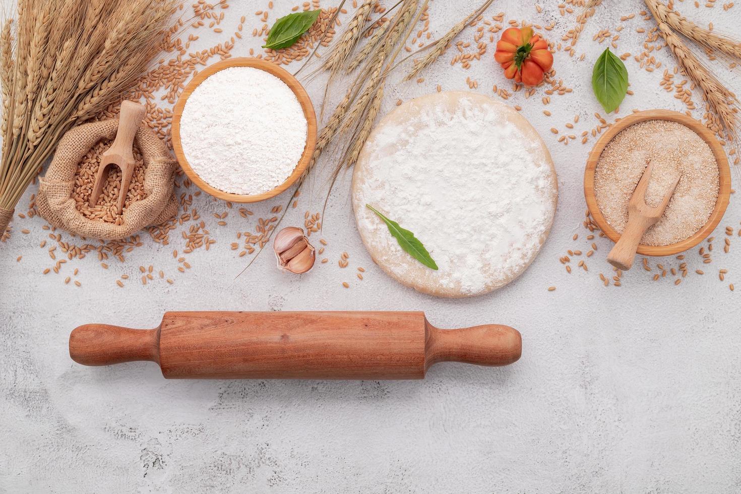 los ingredientes para la masa de pizza casera con espigas de trigo, harina de trigo y granos de trigo sobre fondo de hormigón blanco. foto