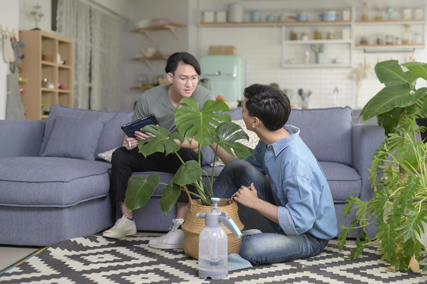 joven pareja gay sonriente cuidando la planta de la casa en la sala de estar en casa, lgbtq y concepto de diversidad. foto