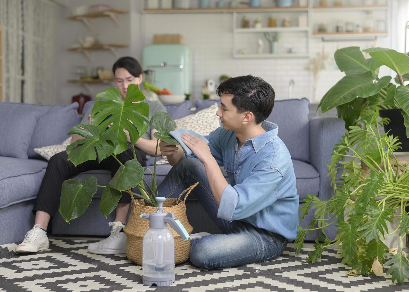 joven pareja gay sonriente cuidando la planta de la casa en la sala de estar en casa, lgbtq y concepto de diversidad. foto