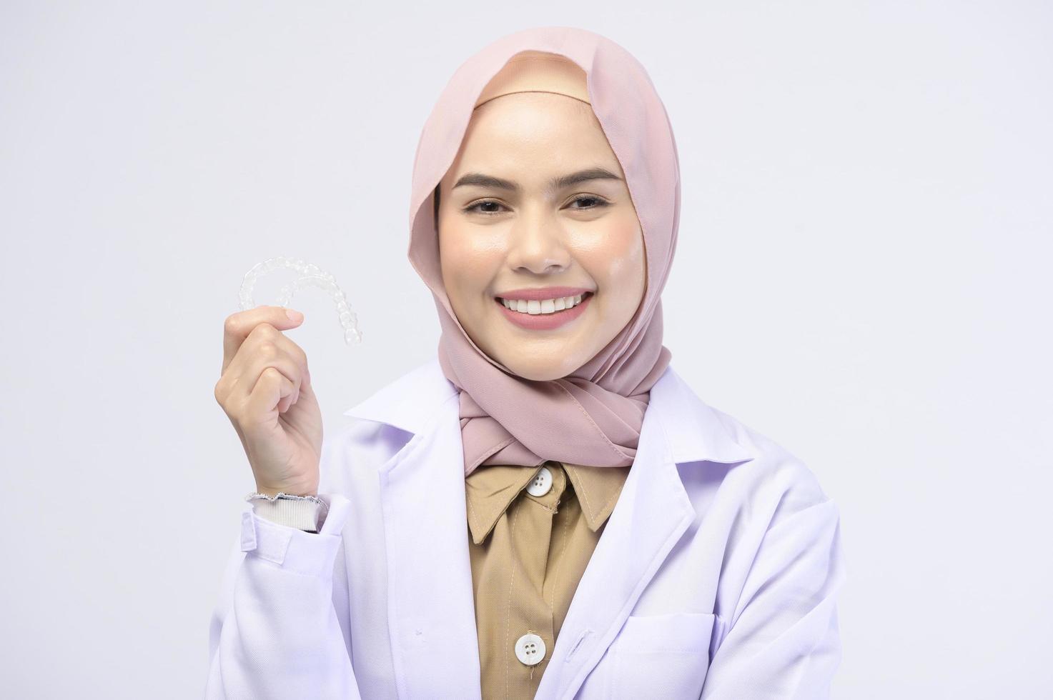 Muslim female dentist holding invisalign braces over white background studio, dental healthcare and Orthodontic concept. photo