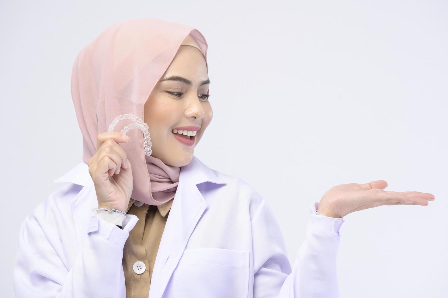 Muslim female dentist holding invisalign braces over white background studio, dental healthcare and Orthodontic concept. photo