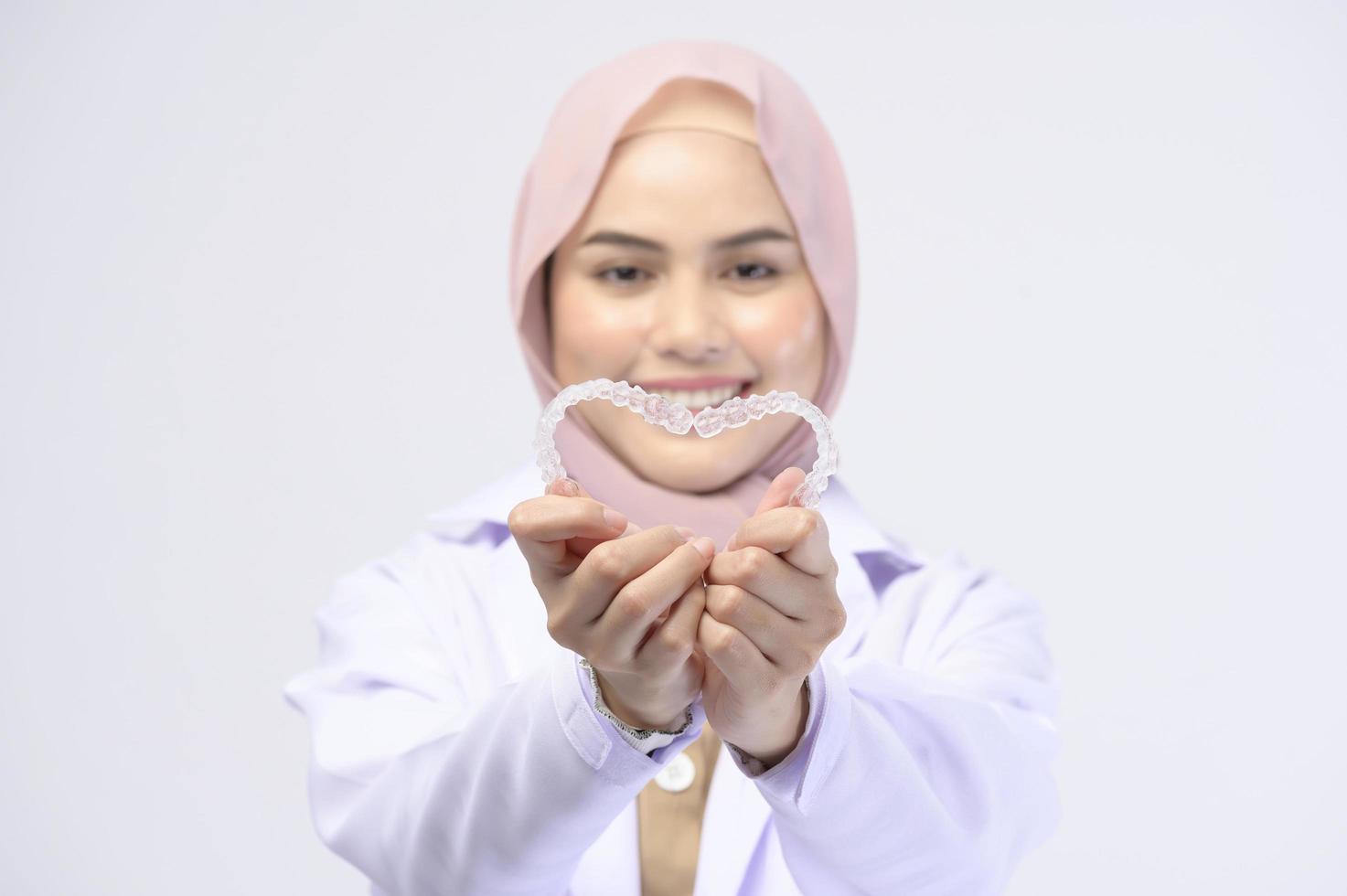 Muslim female dentist holding invisalign braces over white background studio, dental healthcare and Orthodontic concept. photo