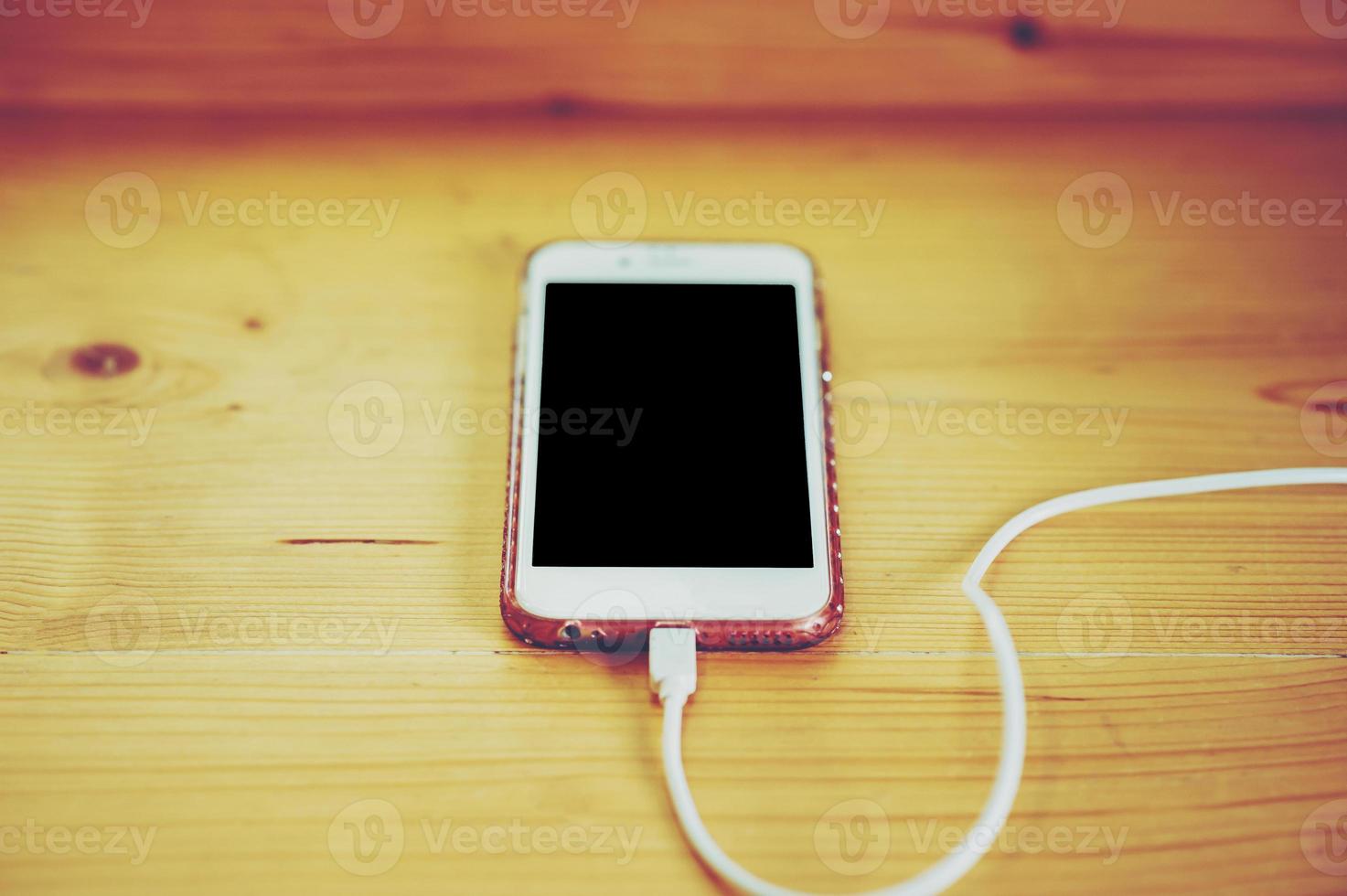 The phone is placed in a wooden table. And plug in the battery because the battery. Communication devices are important in everyday life in this era. photo