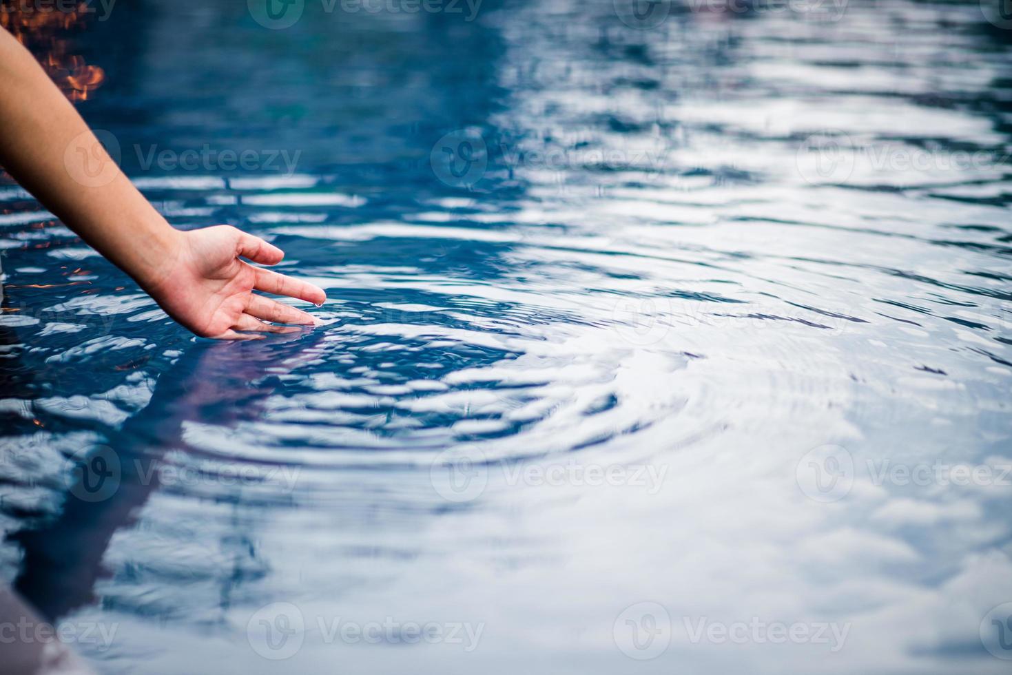 The hand that touches the blue water. The pool is clean and bright. With a drop of water on the water. photo