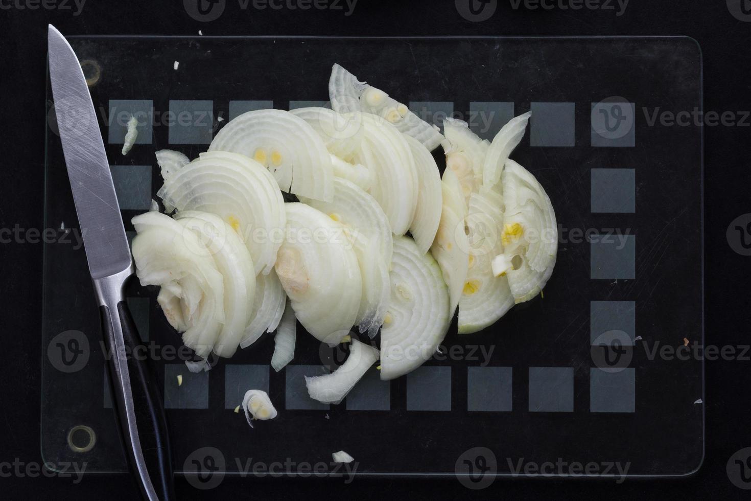 Top view of cutted in half lengthwise onion strips and kitchen knife on the black background photo