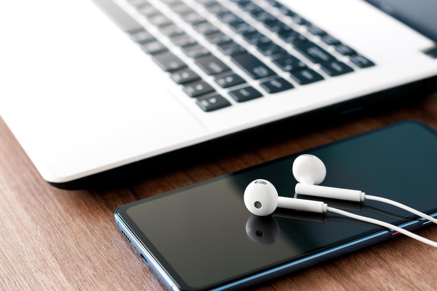 Business working concept, close-up phone earbuds and laptop on wooden table. photo