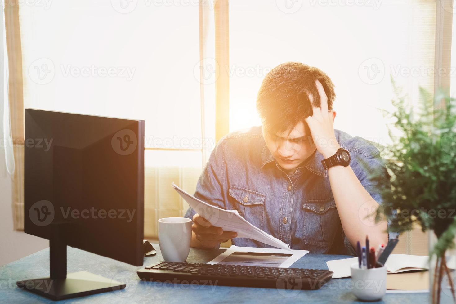 Young Asian men are stressed out in the business office. Looking at the expense bill and the other hand on the head, Thinking of making money to pay off all credit card debts and all bills. photo