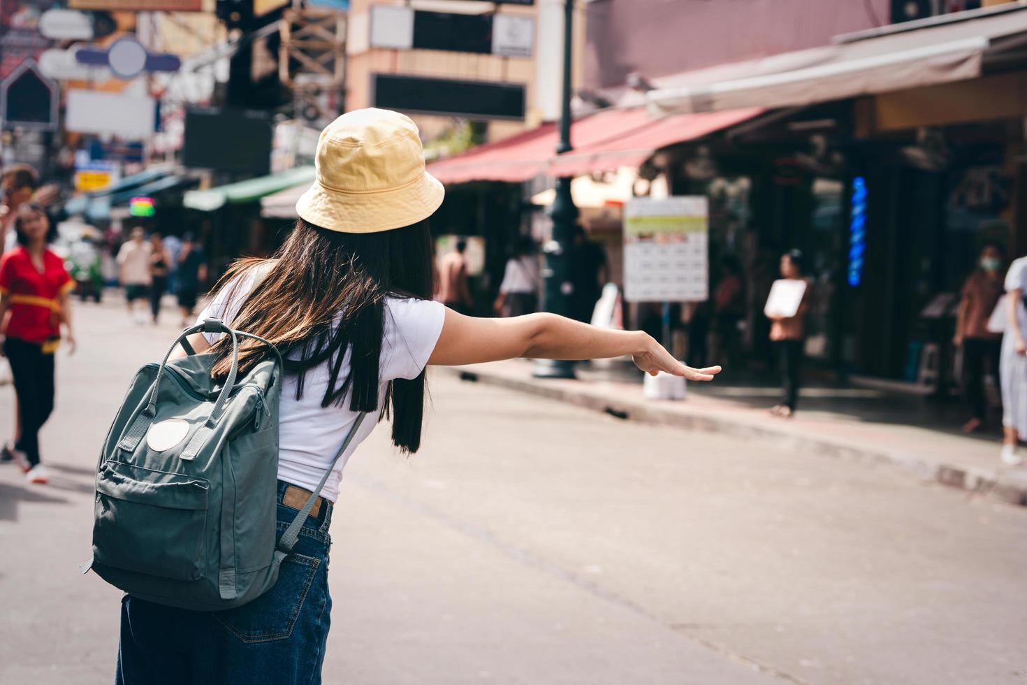 vista posterior mujer asiática llama a un taxi para viajar por la ciudad. foto