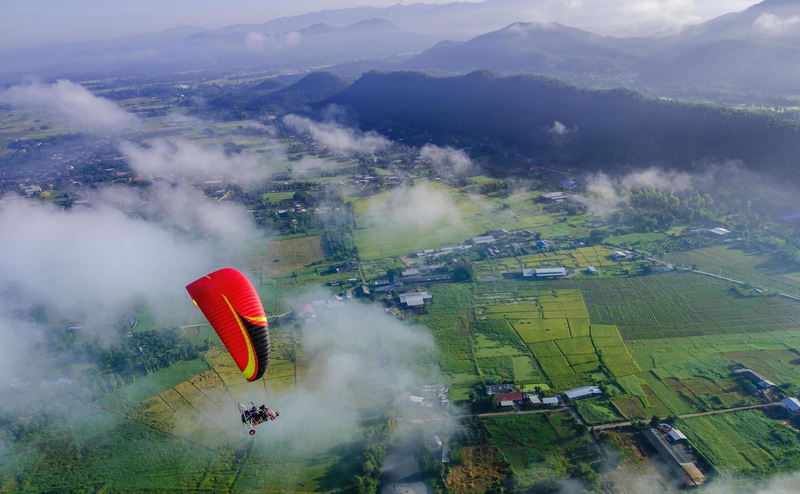 paramotor rojo deslizándose sobre nubes y vastos campos verdes. concepto de libertad. foto