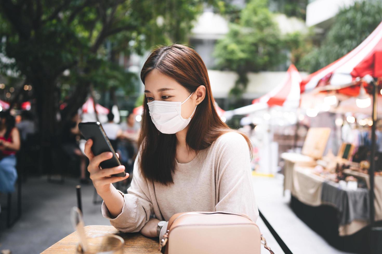 mujer asiática adulta con mascarilla protectora para corona de virus usando la aplicación de teléfono móvil. foto