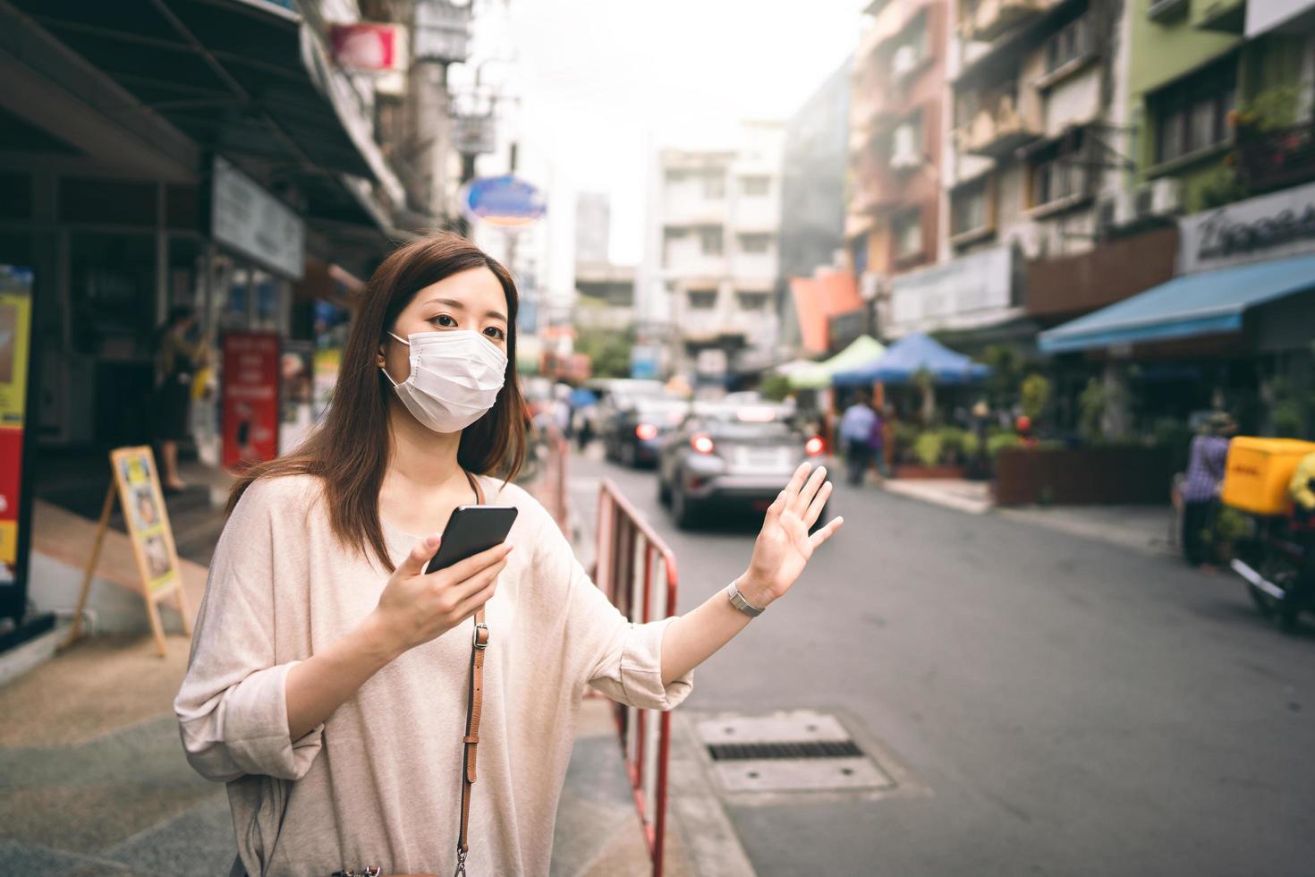 mujer soltera asiática joven de negocios usa mascarilla para proteger el virus de la corona o covid 19 llama a un taxi por aplicación. foto