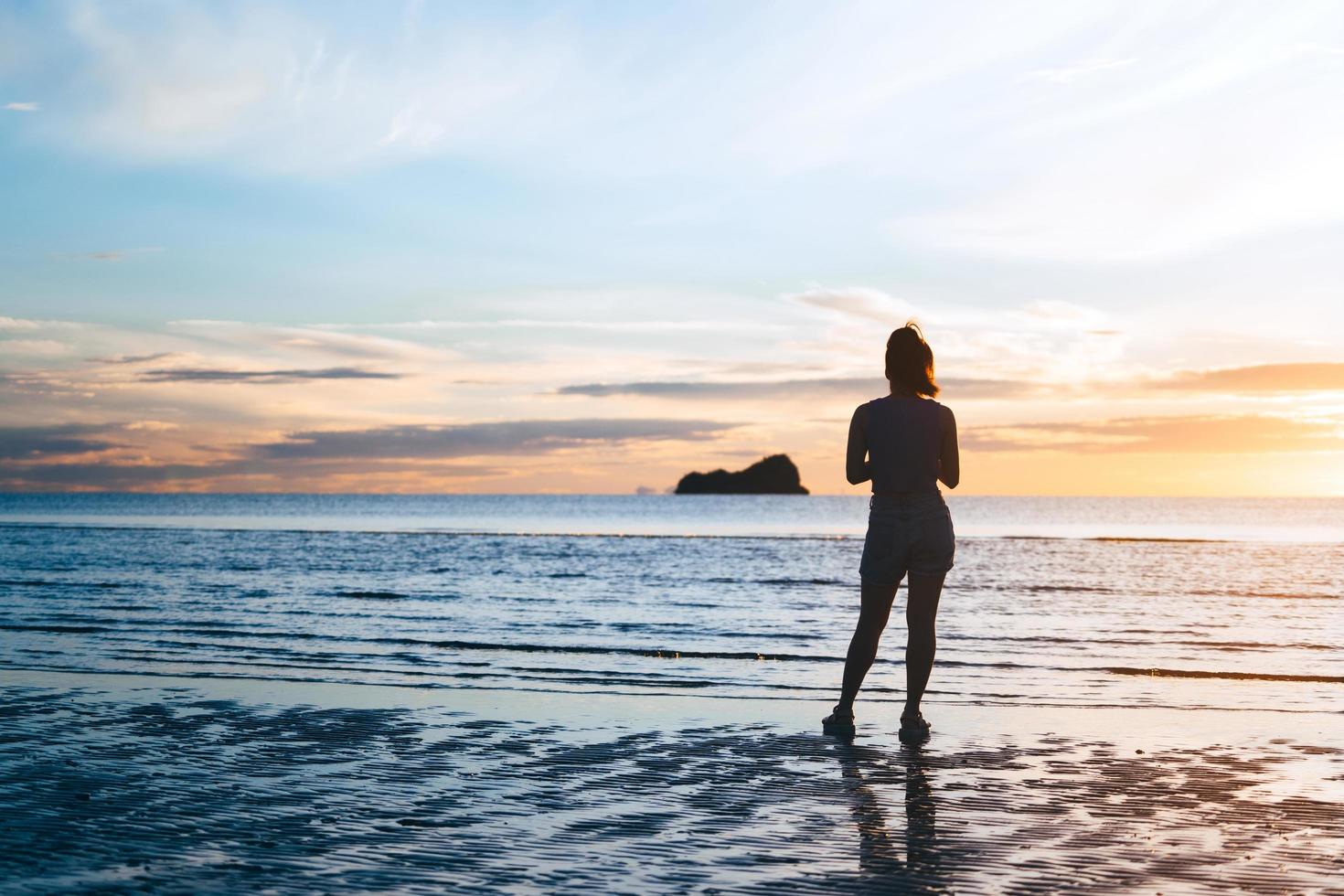 vista trasera de una mujer asiática de viajes adultos jóvenes relajarse en la naturaleza en el mar de la playa con el cielo de la mañana foto