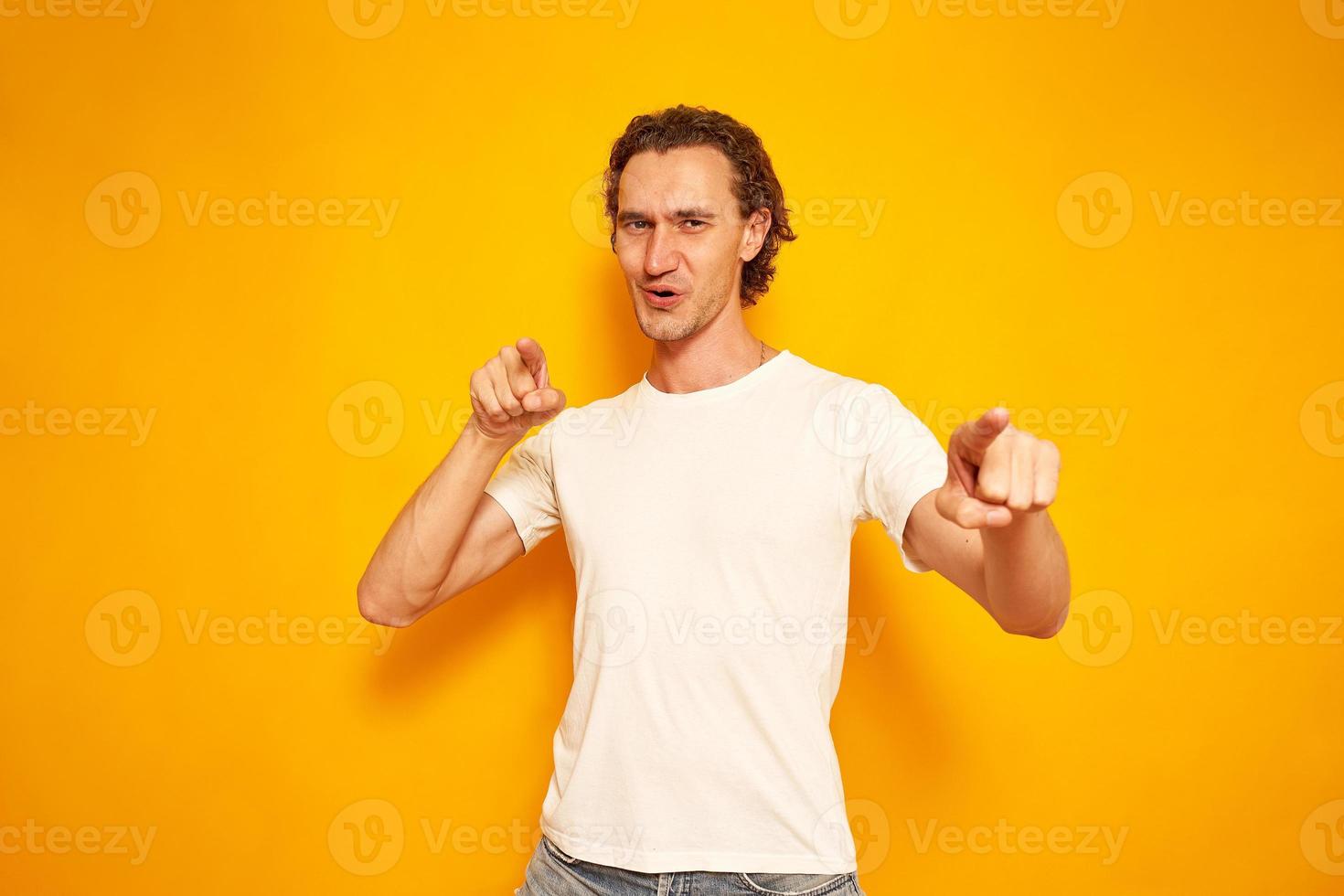 young, joyful, curly-haired man points his index fingers in front of him, hinting that you are best, winner. isolated yellow background with space for text. concept people, victory, advantage, delight photo