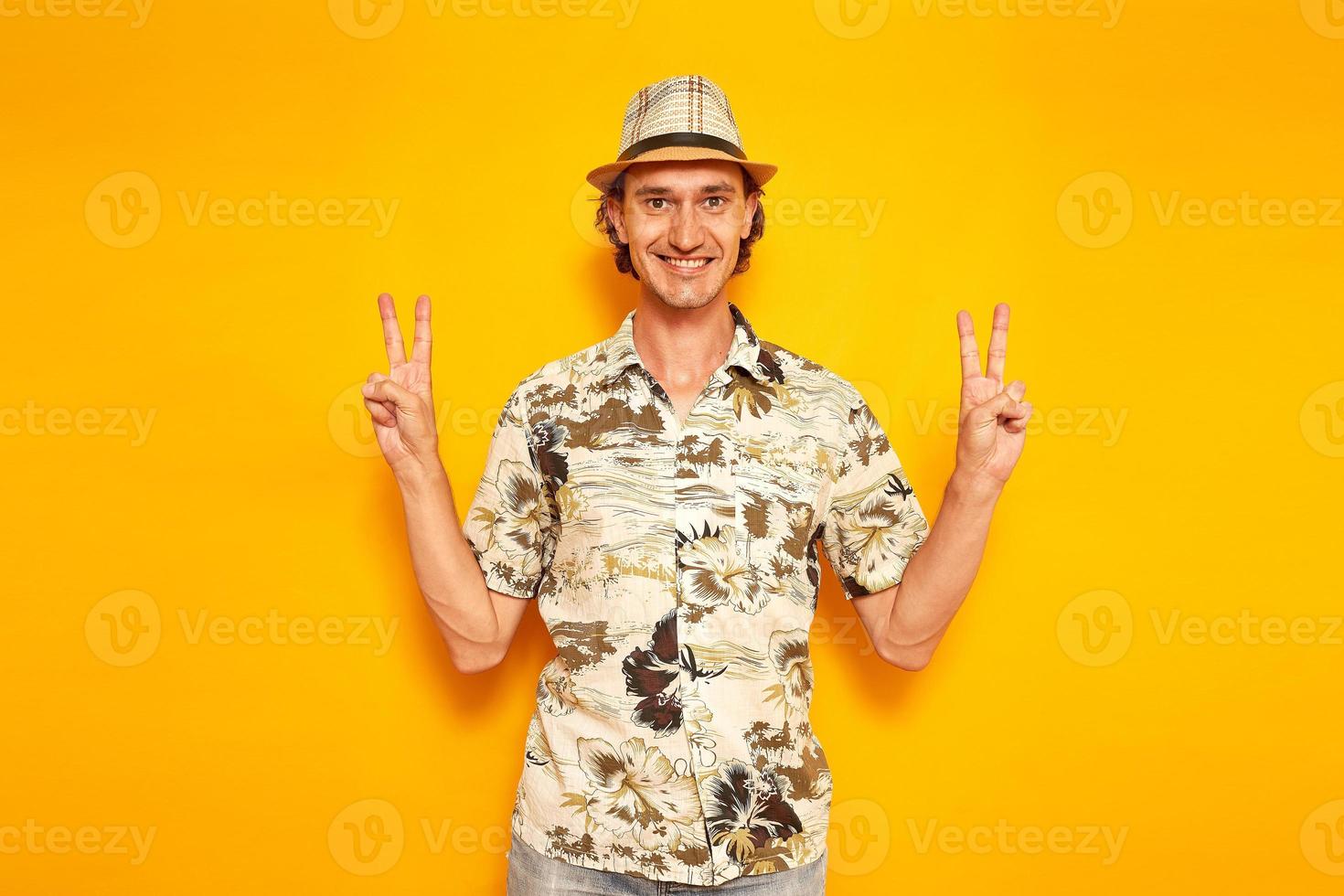 happy smiling male tourist traveler on vacation shows victory sign V, peace with his fingers on his hand. isolated yellow background with space for text. concept - people, adventures, flights abroad photo