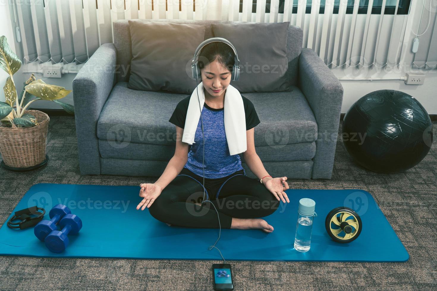 Asian beautiful young woman using smartphone and headphones while meditating and practicing yoga at home. photo
