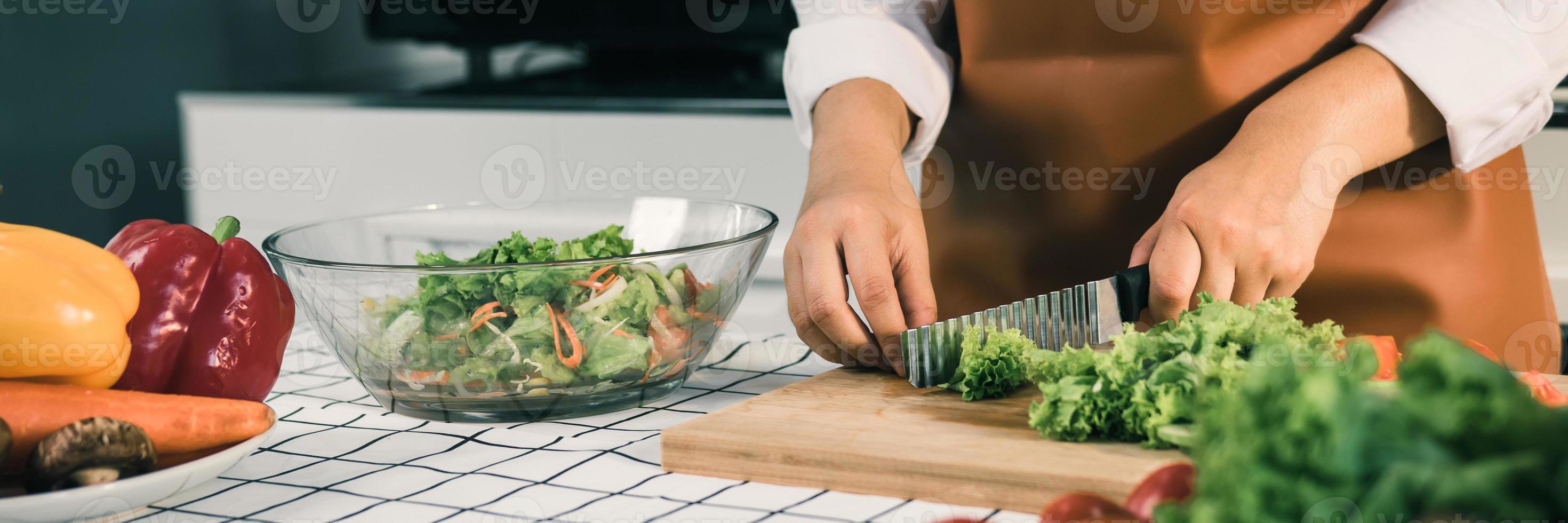 Asian woman uses a knife to cut the salad greens in the kitchen. photo