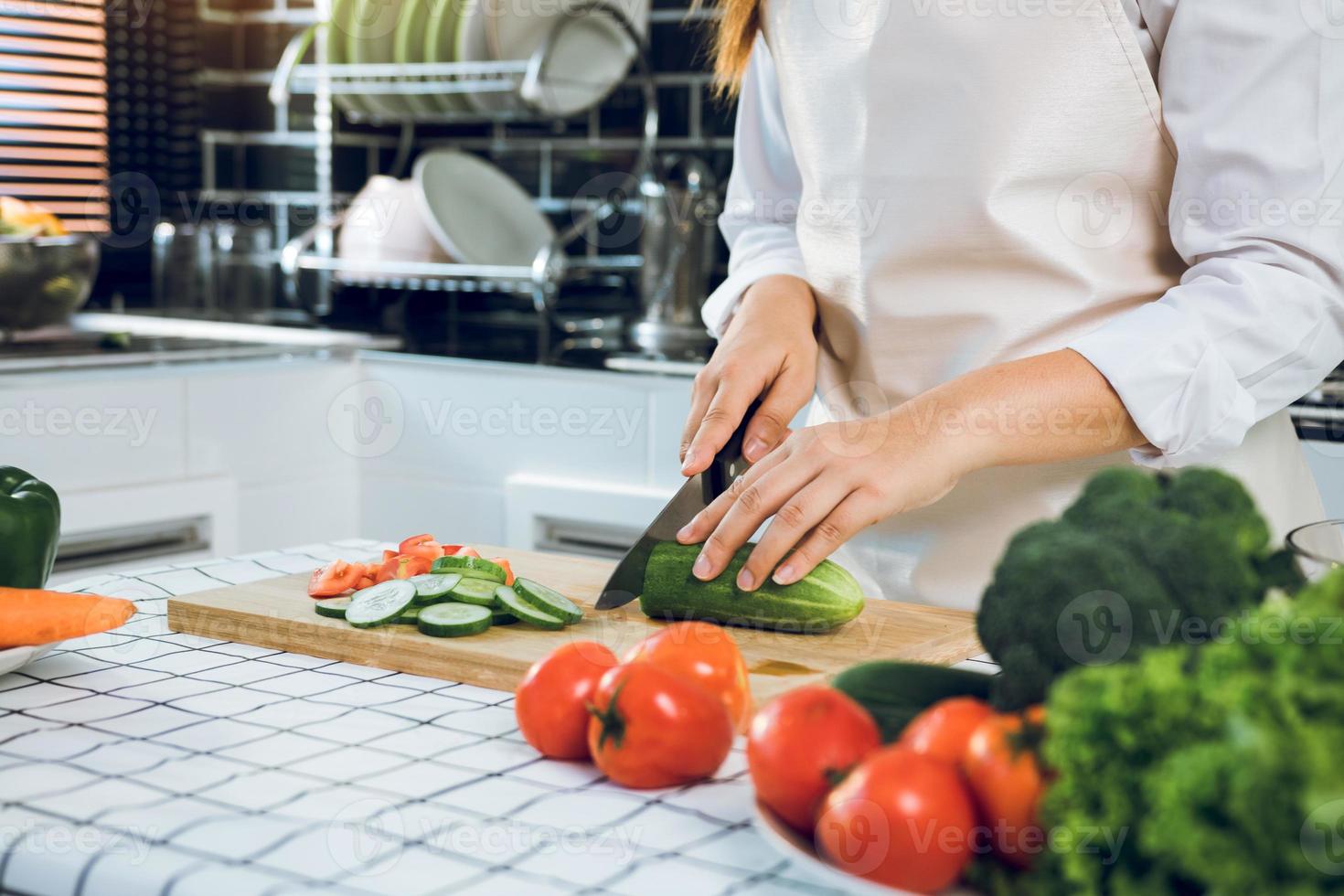 Woman using knife and hands cutting cucumber on wooden board in kitchen room. photo