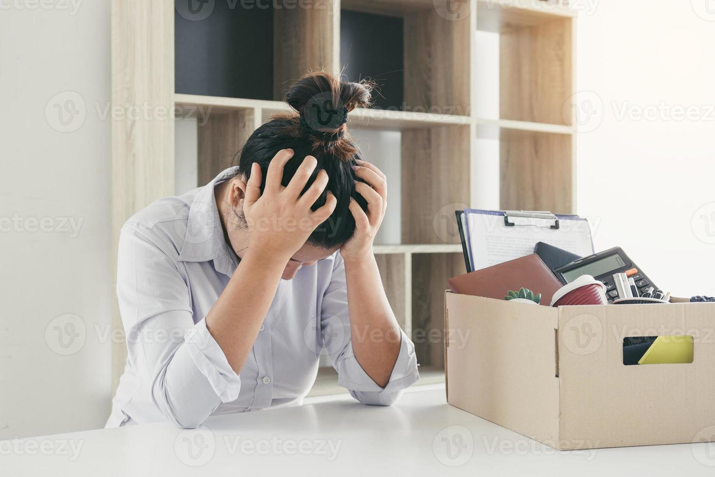 Woman employee used his hand to hold the head feeling sad at his desk when he received the contract envelope for resigning from the company. photo