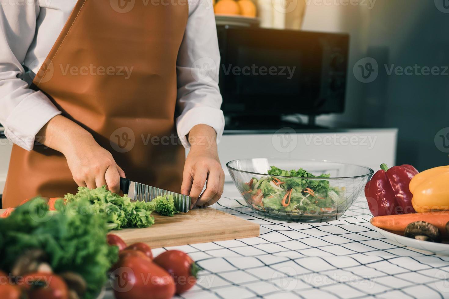 mujer asiática usa un cuchillo para cortar las verduras de ensalada en la cocina. foto