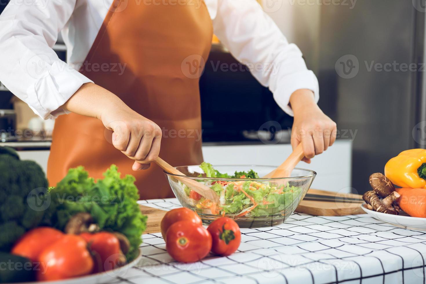Asian woman is mixing the ingredients in a salad bowl at the kitchen cooking table. photo