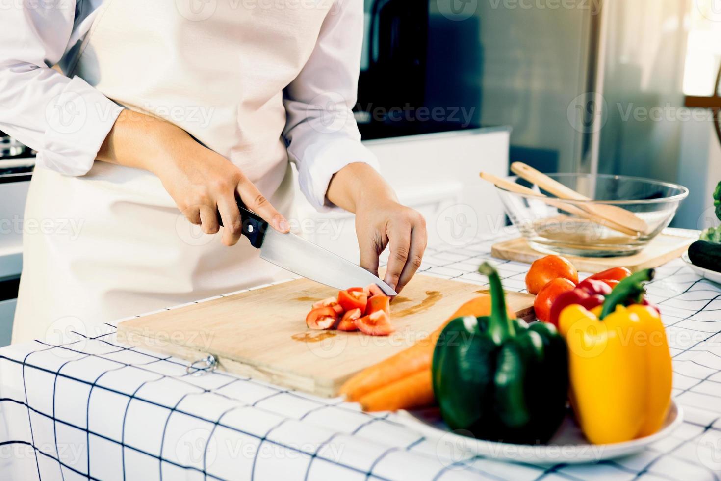 Woman using knife and hands cutting tomato on wooden board in kitchen room. photo