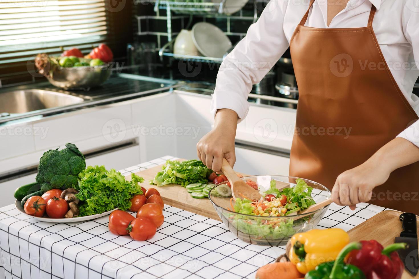 Asian woman is mixing the ingredients in a salad bowl at the kitchen cooking table. photo