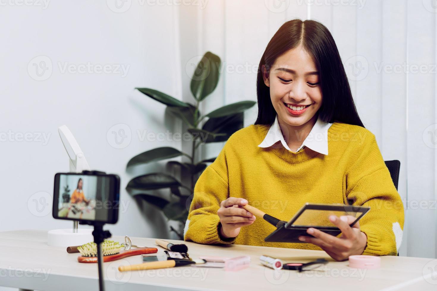 una joven asiática vlogueando sobre productos de belleza haciendo un video para su blog sobre cosméticos usando una cámara de teléfono en casa. foto