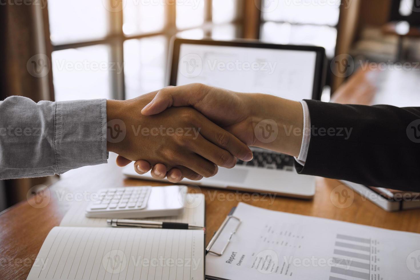 Entrepreneurs collaboration deal shaking hands in a modern office and financial paper graph on desk. photo