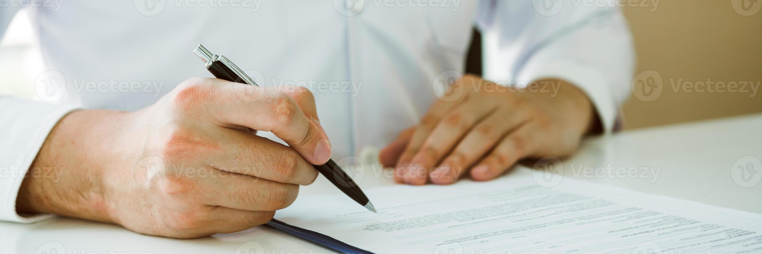 Doctor hand holding pen writing patient history list on note pad and talking to the patient about medication and treatment. photo