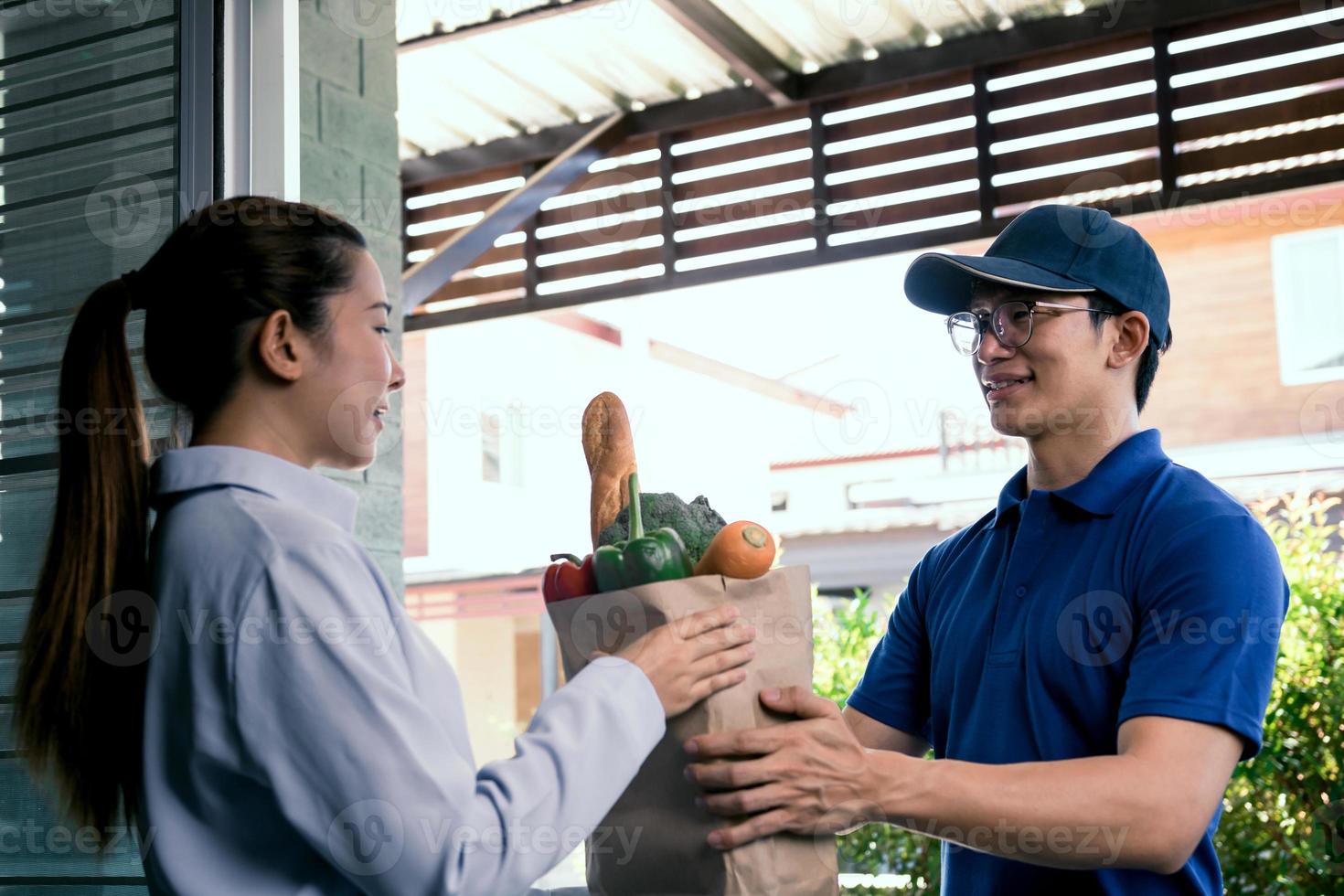 Delivery asian man handing a paper bag inside with vegetables or food to an Asian woman in front of his house. photo