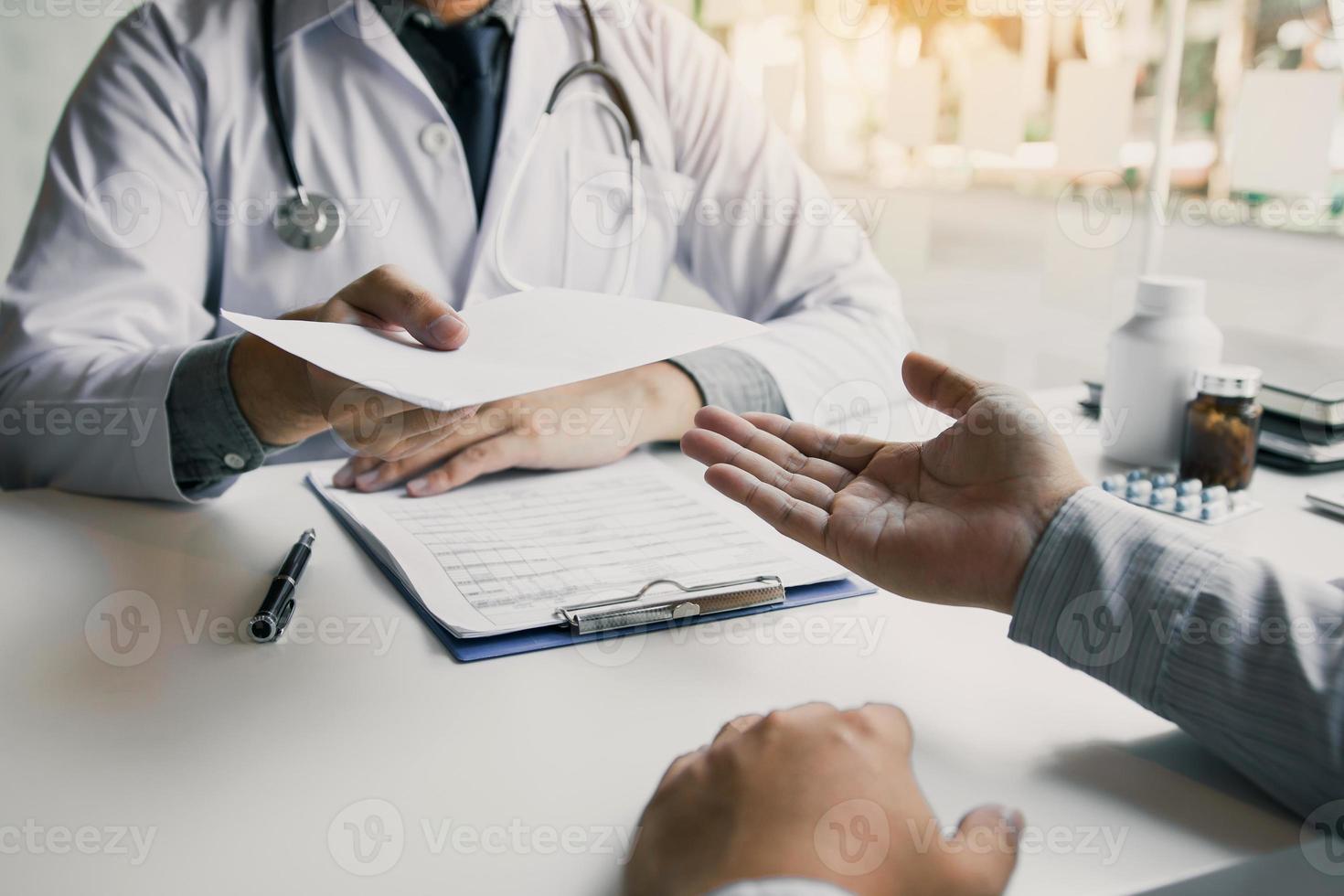 Asian male doctor talking in clinic room and handing a prescription to the patient. photo