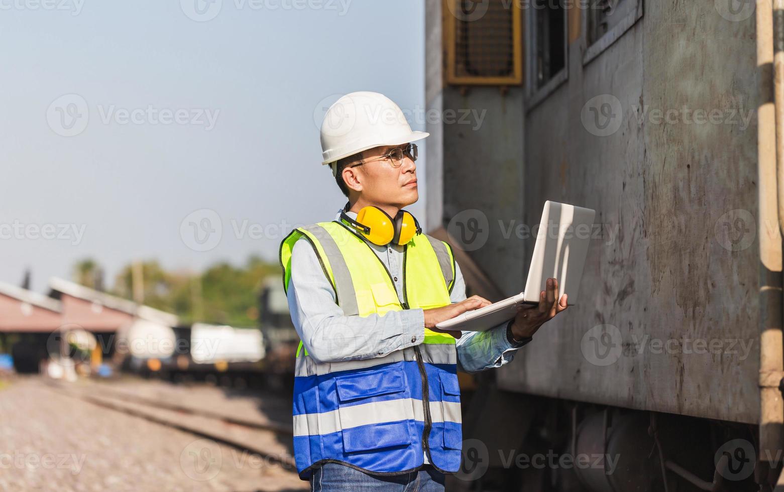 Engineer man in waistcoats and hardhats with laptop in a railway depot, Engineer under inspection and checking construction process railway locomotive repair plant photo