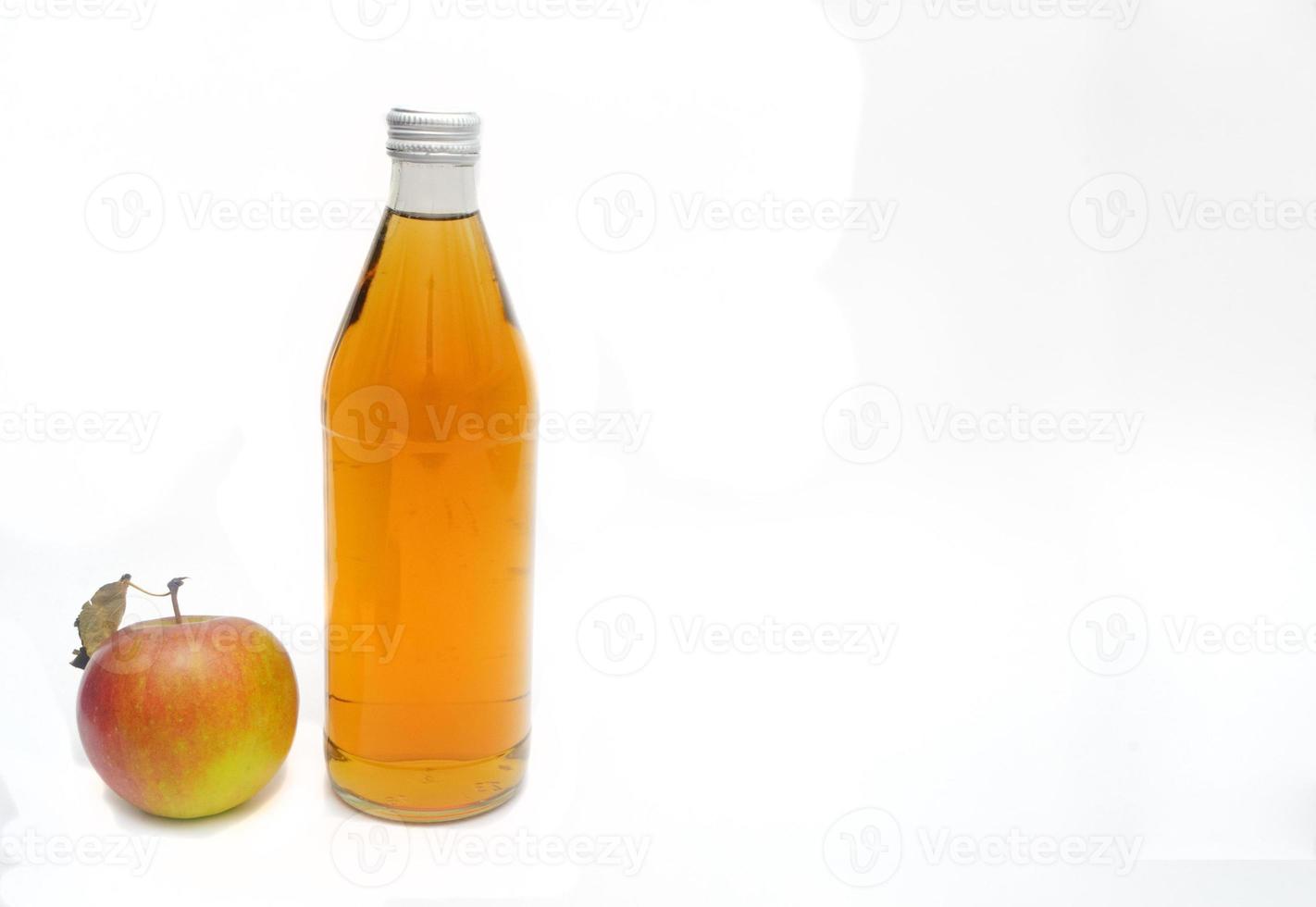 Una manzana entera con hojas y una botella de vinagre de sidra de manzana con fondo blanco, espacio de copia. foto